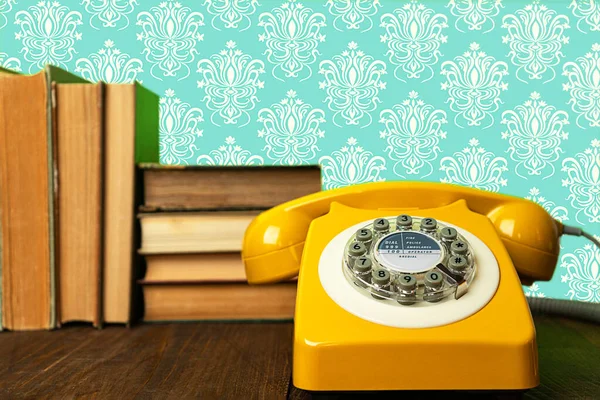 Teléfono amarillo retro sobre mesa de madera con libros antiguos y fondo abstracto . — Foto de Stock