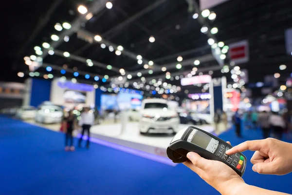 Máquina de tarjeta de crédito de mano en la foto borrosa del espectáculo de automóviles, sala de exposición de coches Imagen de archivo