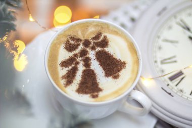 Süt köpüğünde çan desenleri olan beyaz bir bardaktaki Noel kapuçinosunun arka planı.