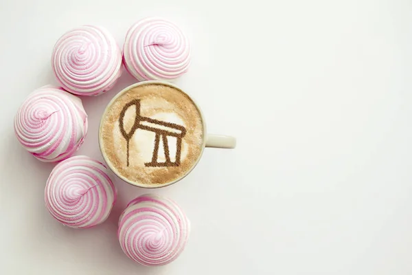 a cup of cappuccino coffee with a drawing of an oil producing tower from cinnamon on milk foam