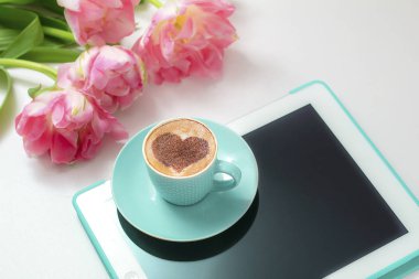  Sıcak kahve cappuccino ile latte romantik kalp sanatı. Pembe laleler ve tablet bilgisayar 