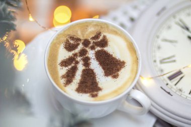 Süt köpüğünde çan desenleri olan beyaz bir bardaktaki Noel kapuçinosunun arka planı.