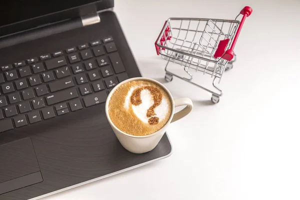 coffee cappuccino with question mark on milky foam near the laptop and shopping basket