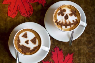 İki bardak kapuçino, üzerinde cadılar bayramı sembolü sütlü latte sanatı.