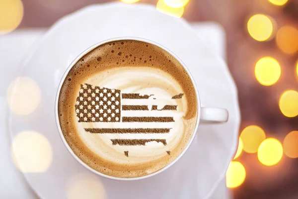 Flag of the United States of America in the form of territorial borders on a cappuccino coffee cup close-up