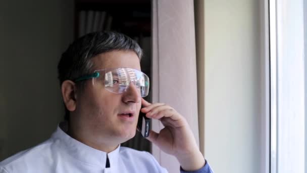 El médico habla por teléfono móvil y mirando por la ventana — Vídeo de stock