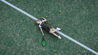 Kız tenis kortunda yatıyor.