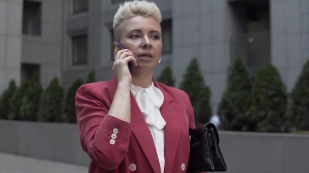 路上で携帯電話で話している彼女の手の中に袋と赤いジャケットのビジネス女性 — ストック動画