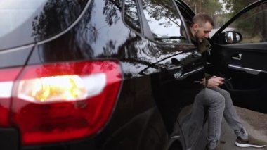 Bir adam bozuk bir arabada oturur ve telefonda yazar.