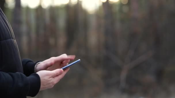 一个人在森林的后面用了一部电话 夕阳西下的光线穿过了它 — 图库视频影像