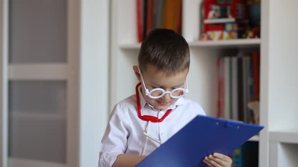 一个戴着玩具眼镜扮演医生角色的孩子在他的剪贴板上记笔记 — 图库视频影像