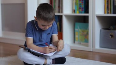 Çocuk odada yere oturmuş bir albüm çiziyor.