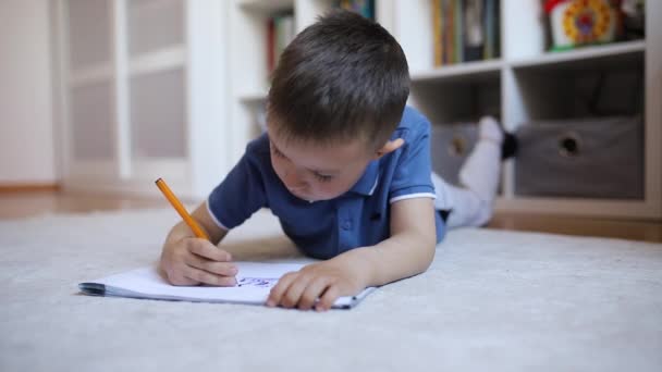 Мальчик Рисует Альбом Лежа Ковре Комнате Своего Ребенка — стоковое видео