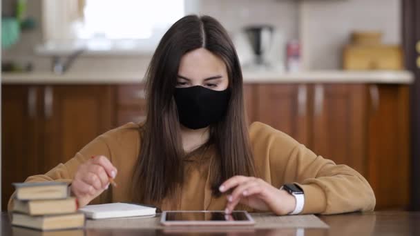 Girl in a respiratory mask is typing on a tablet while sitting at home