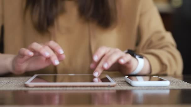 一个穿着棕色毛衣的女孩坐在厨房的桌子旁边 一边在平板电脑上打字 另一边是一部手机 — 图库视频影像