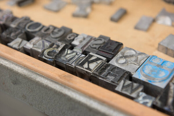 Vintage lead letterpress printing blocks against a weathered wooden drawer background with bokeh.