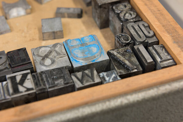 Vintage lead letterpress printing blocks against a weathered wooden drawer background with bokeh.