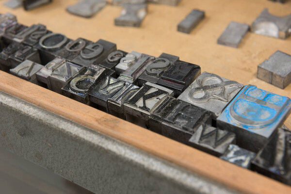 Vintage lead letterpress printing blocks against a weathered wooden drawer background with bokeh.