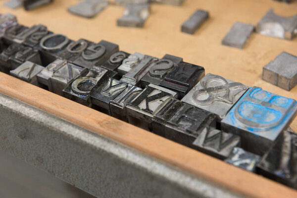 Vintage lead letterpress printing blocks against a weathered wooden drawer background with bokeh.