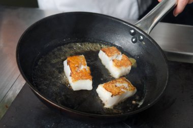 Pan fried golden fish fillet cubes, frying in real butter, in a non stick rustic pan. clipart