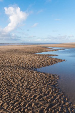 Güzel mavi gökyüzü ve dokulu kum, plajda serin güneşli kışlar gününde