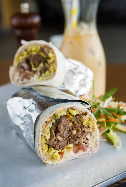 Mexican shredded beef breakfast burrito sliced in half served with ice coffee.