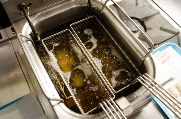 A silver deep pan industrial kitchen oil fryer, with golden oil, bubbling and frying potatoes