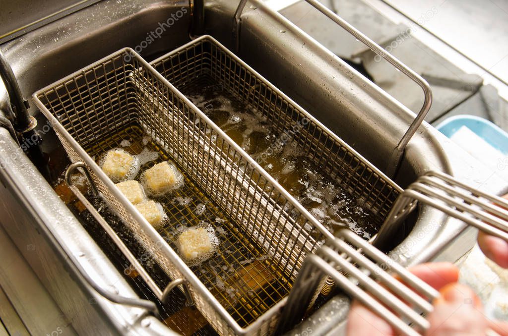 A silver deep pan industrial kitchen oil fryer, with golden oil, bubbling and frying potatoes