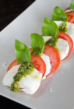 Caprese salatası, asma ripetomato ve mozzarella peyniri dilimleri fesleğen yaprakları ve taze yeşil pesto ile.