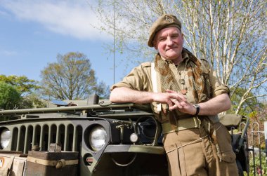 Yorkshire, İngiltere, 05 / 15 / 2015, Bere şapkalı bir İngiliz savaş gazisi bir asker bir ordu cipine yaslanıyor. Howarth 1940 'ların hafta sonu