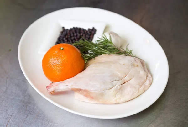 Free range raw duck leg, with herbs, orange and garlic, on a white plate. Duck wellington step by step.
