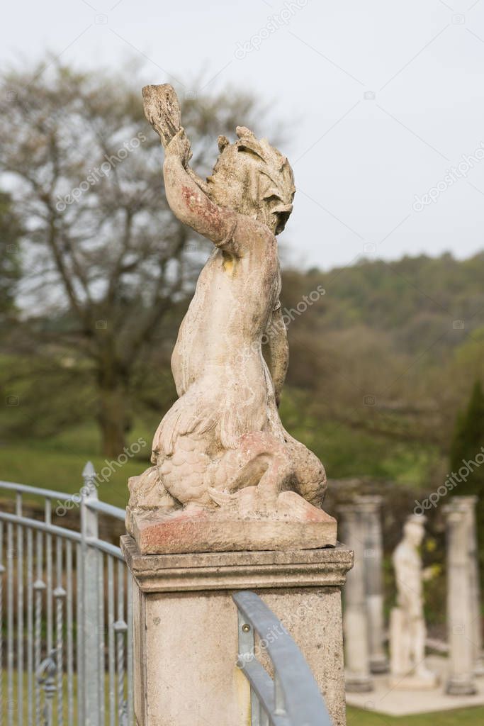 A hand carved cherub blowing a horn. A roman style stone carved statue, on a stone base