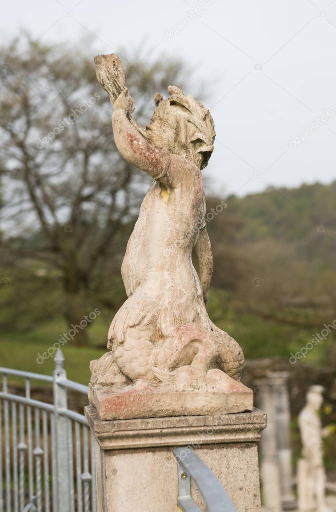 A hand carved cherub blowing a horn. A roman style stone carved statue, on a stone base