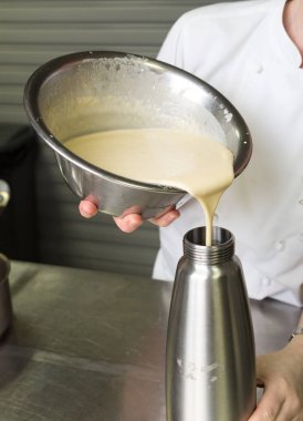 Kalın taze tatlı tatlı krema, bir endüstriyel mutfak metal bir kaba dökülür varlık.