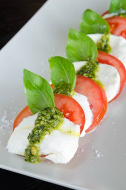 Caprese salatası, asma ripetomato ve mozzarella peyniri dilimleri fesleğen yaprakları ve taze yeşil pesto ile.