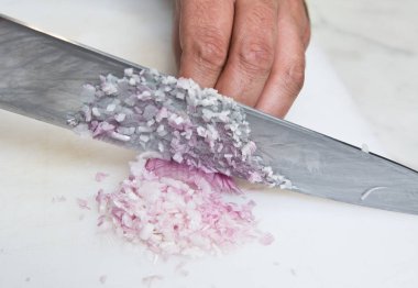 Taze organik arpacık, beyaz kesme tahtası üzerinde dicing bir bıçak.