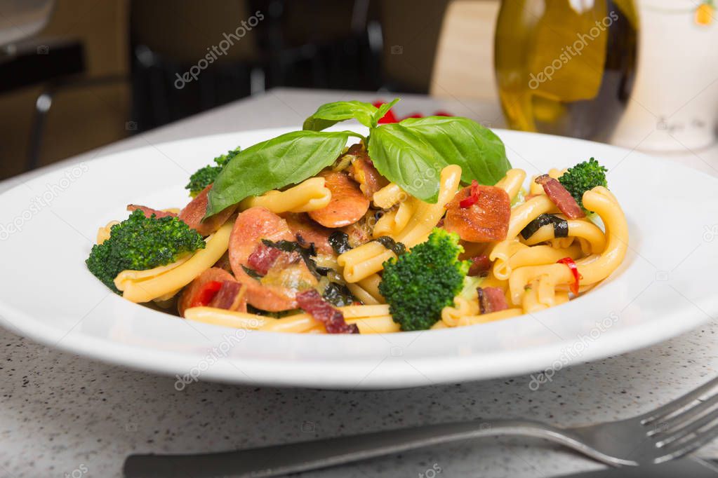 A delicious fresh gourmet Italian strozzapreti pasta dish, with pancetta, italian sausage, broccoli, vegetables, topped with fresh basil.