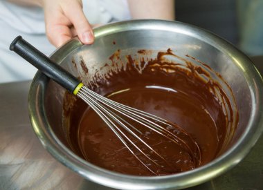 Bir metal kase ve çırpma teli ile zengin kalın koyu eritilmiş çikolata sosu, metal bir endüstriyel mutfak.