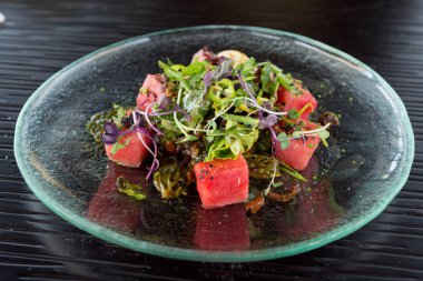 Bir baharatlı sos ile drizzled bir serinletici karpuz, kırmızı biber, tere ve marul salatası, çağdaş cam tabakta