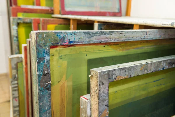 Silk screen printing screens stored in a wooden rack ready for printing.