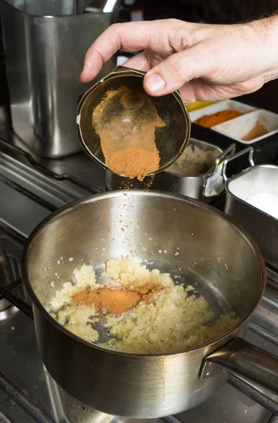 Куркума порошок падает в кастрюлю с жареным чесноком и мелко нарезанным луком. Шаг за шагом рецепт приготовления пищи . — стоковое фото