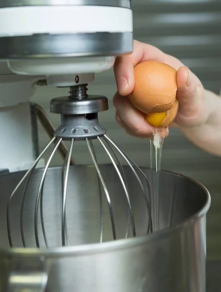 A fresh free range egg being cracked into an industrial metal whisking machine. Shot with a shallow depth of field.