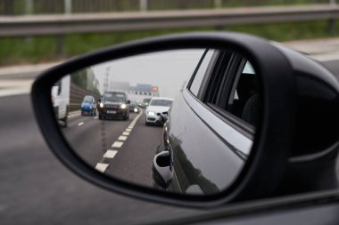 Bir otoyolun dikiz aynasından görünen dikiz aynası bir otomobil otomobilinde. Kasvetli, kirli şehir gökyüzü ve araç arka planı. Şehir sokaklarında hızlı araba kullanmak..