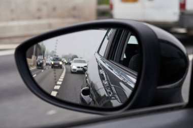 Bir otoyolun dikiz aynasından görünen dikiz aynası bir otomobil otomobilinde. Kasvetli, kirli şehir gökyüzü ve araç arka planı. Şehir sokaklarında hızlı araba kullanmak..