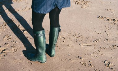 Plajda yürüyen lastik çizme giyen bir çift ayak. Su geçirmez ayakkabılar dağlarda ve nehirlerde sahilde yürümek için. Zihinsel sağlık ve fiziksel refah için egzersiz. 