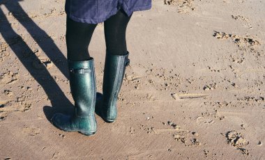 Plajda yürüyen lastik çizme giyen bir çift ayak. Su geçirmez ayakkabılar dağlarda ve nehirlerde sahilde yürümek için. Zihinsel sağlık ve fiziksel refah için egzersiz. 