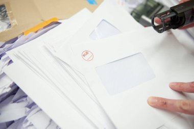 Önünde para pulu olan boş beyaz bir zarf. Ödenmiş zarf faturalarını damgalayan bir el. Ofis ve iş malzemeleri, ödenmiş faturalar..