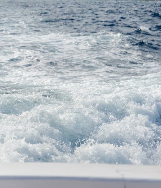 Mavi okyanustaki bir teknenin arkasından su sıçrıyor ve dalgalanmalar oluyor. Tekne hareketi ve hareket, kaynayan su yüzeyi. İlerleme kaydediyor ve geride bırakıyor,