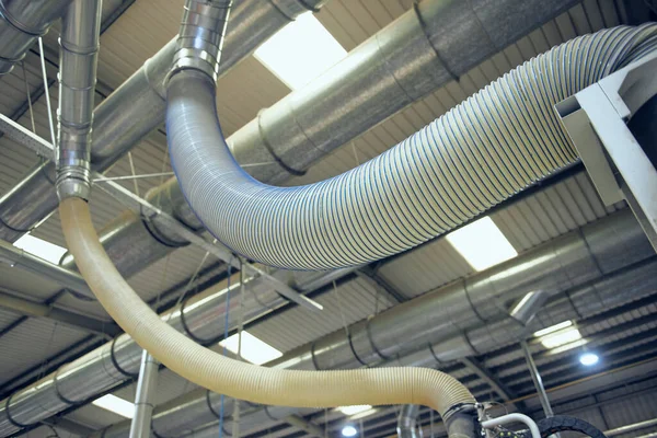 Plastic ribbed air conditioning airflow pipes and tubing sucking dust and industrial particles out of wood and metal cutting machines. Keeping the air and workplace clean and free from environmental pollution.
