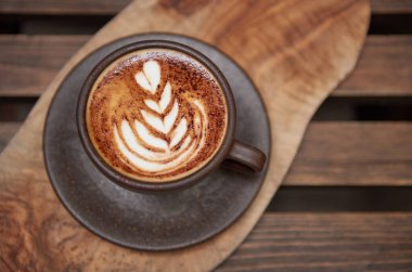 Kremalı kahveyle dolu güzel, kahverengimsi, sıcak bir kahve fincanı. Kahveli, ahşap bir kahve dükkanında servis ediliyor. Organik adil ticaret kahvesi yukarıdan çekilmiş.